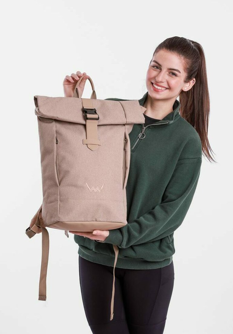 Beige canvas backpack with a roll-top closure, tan accents, adjustable straps, and a subtle logo embroidery on the front.