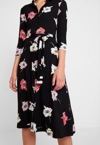 Black floral dress with three-quarter sleeves, button front, and belted waist. Features colorful flowers in pink, red, white, and yellow.