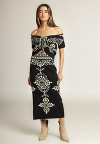 Conjunto de dos piezas de punto negro que incluye un top con hombros al descubierto y un detalle de lazo en la parte delantera, junto con una falda de longitud hasta la rodilla con patrones florales blancos.