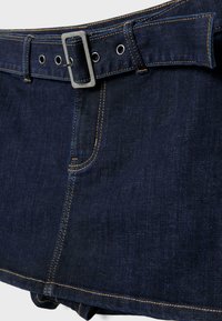 Mørkeblå denimnederdel med orange syning og bælte i matchende farve med et rektangulært sølvspænde og metal-øjer.