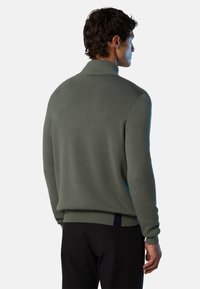 Maglione verde lavorato a maglia con colletto alto, polsini a coste e orlo. Presenta una finitura testurizzata e un accento blu a contrasto sul retro.