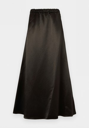 Γυναίκα που στέκεται, φορώντας ένα ανοιχτό μπλε φαρδύ πουκάμισο με κουμπιά, σκούρα καφέ μακριά φούστα και κρεμ μυτερά τακούνια σε απλό φόντο.