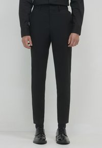 Pantaloni neri su misura con un design slim fit, realizzati in tessuto morbido, dotati di passanti per cintura e abbinati a scarpe eleganti nere lucide.