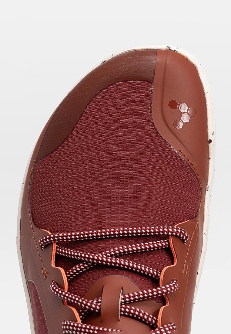 Zapatilla de tela color marrón con superposiciones sintéticas texturizadas, suela moteada en blanco y cordones en contraste de color marrón y blanco. Presenta un emblema de marca.