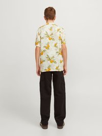 Camicia a maniche corte e colletto con sfondo bianco e motivo di frutti arancioni; pantaloni cargo neri con tasche laterali; scarpe marroni.