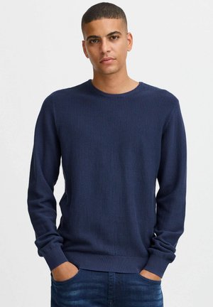 Marinblå stickad tröja med texturerad design, rund hals och långa ärmar. Muddarna och fållen har ribbade detaljer. Bärs med blå jeans.
