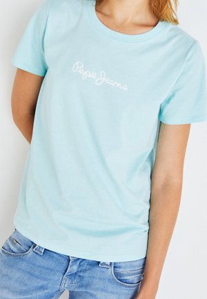 Personne portant un t-shirt Pepe Jeans bleu clair à manches courtes et un jean denim bleu sur un fond blanc uni.