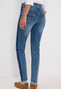 Blå denim jeans med slim fit, blekt mönster och två bakfickor. Accenterad med ett kontrasterande mörkt rand längs sömmen på sidan.