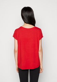 Rød t-shirt med korte ærmer og rund halsudskæring. Blødt, let stof. Løs pasform med længere bagstykke. Sorte bukser bæres nedenunder.