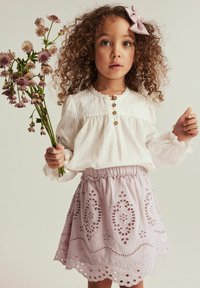 Weiß gestreifte Bluse mit Puffärmeln und Holzknöpfen, kombiniert mit einem lavendelfarbenen bestickten Rock mit Lochmuster und einem Rüschensaum.