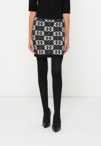 Mini saia preta e branca com padrão, cós canelado, combinada com collants pretos e saltos altos de bico fino.