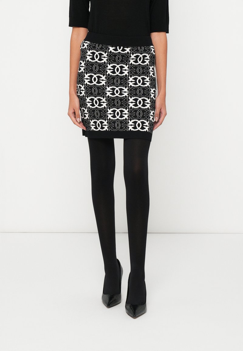 Mini saia preta e branca com padrão, cós canelado, combinada com collants pretos e saltos altos de bico fino.