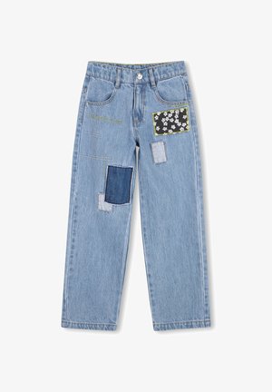 Jean en denim bleu clair avec plusieurs patchs de formes et couleurs variées, comprenant un tissu fleuri noir et des détails de couture contrastants.