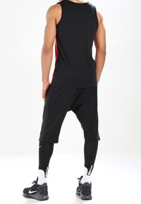 Camiseta atlética negra sin mangas con acentos laterales rojos, combinada con pantalones cortos negros y leggins negros. Presenta la marca Nike en las zapatillas y en los calcetines.