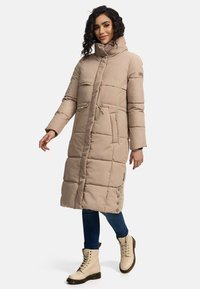 Beige puffer coat with a high collar, quilted design, zip pockets, and side button accents; paired with light-colored lace-up boots.