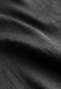 Black fabric with a smooth texture and subtle sheen, featuring soft folds and slight variations in light and shadow.