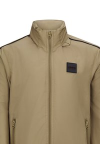 Beige zip-up jack met een hoge kraag, zwarte accenten op de schouders, twee zijzakken en een vierkante logo-patch op de borst.
