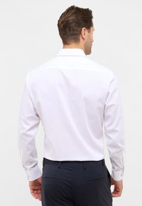 Witte langmouwige overhemd met een gladde textuur en een klassieke kraag, gecombineerd met marineblauwe broek. Heeft knoopmanchetten en een aansluitend ontwerp.