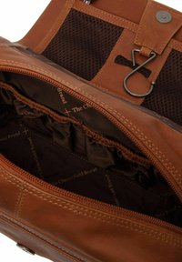 Intérieur d'un sac en cuir marron comprenant une poche zippée, un panneau en maille noire et une doublure avec logo et détails plissés, mettant en valeur le savoir-faire.