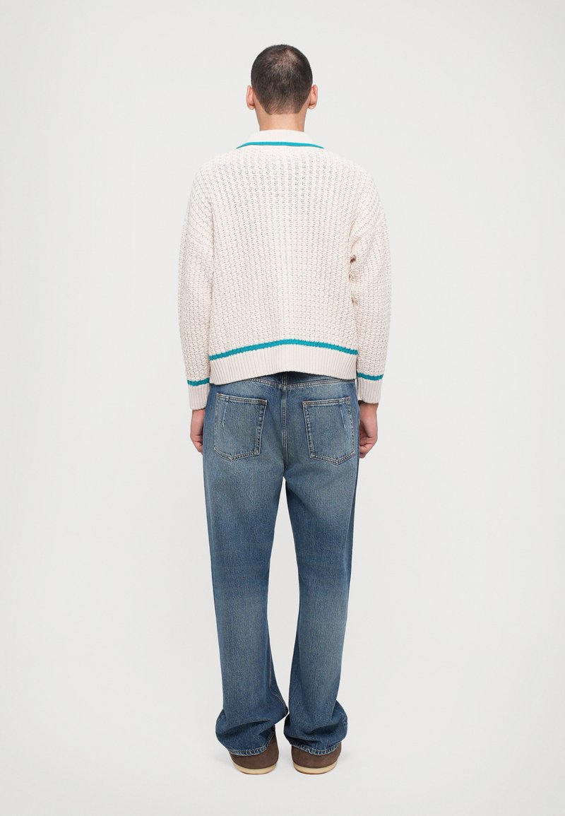 Chunky knitted cream cardigan with turquoise accents, paired with loose-fitting blue denim jeans, viewed from the back.