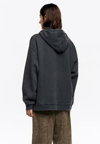 Przewymiarowana bluza z kapturem w kolorze węgielnym, z troczkami przy kapturze, prążkowanymi mankietami i ściągaczem u dołu. Materiał wydaje się miękki, o delikatnie zużytej fakturze.