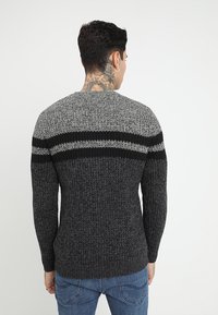 Maglione grigio scuro lavorato a maglia con accenti a righe in grigio chiaro e nero, con scollo tondo e maniche lunghe.