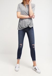 Gray short-sleeve t-shirt with a knotted front, paired with dark blue skinny jeans featuring ripped detailing, and white sneakers with black stripes.
