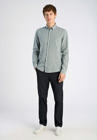 Camisa de botones a rayas verde claro con cuello, bolsillo en el pecho, combinada con pantalones negros y zapatillas blancas. Textura de tela suave.