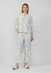 Blouse bleu clair avec un décolleté en V et des manches trois-quarts, associée à un pantalon à jambes larges, le tout ornée d'un motif floral en beige doux et crème.