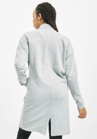 Sweatshirt lung gri cu guler înalt, mâneci lungi și o fante pe spate. Material texturat, moale, cu detalii de cusături minime.