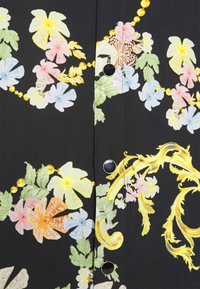 Tessuto a fantasia floreale con fiori multicolori e foglie verdi su uno sfondo nero, con accenti decorativi gialli e bottoni neri.