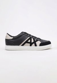 Zapatillas negras y beige con parte superior de cuero suave, acentos de ante en contraste, suela de goma blanca y un destacado logo en el lateral.