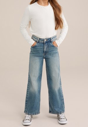 Bredbenede blå denimjeans med højtaljet design, der har en klassisk fem-lomme konstruktion og en front-knaplukning, kombineret med en hvid langærmet top.