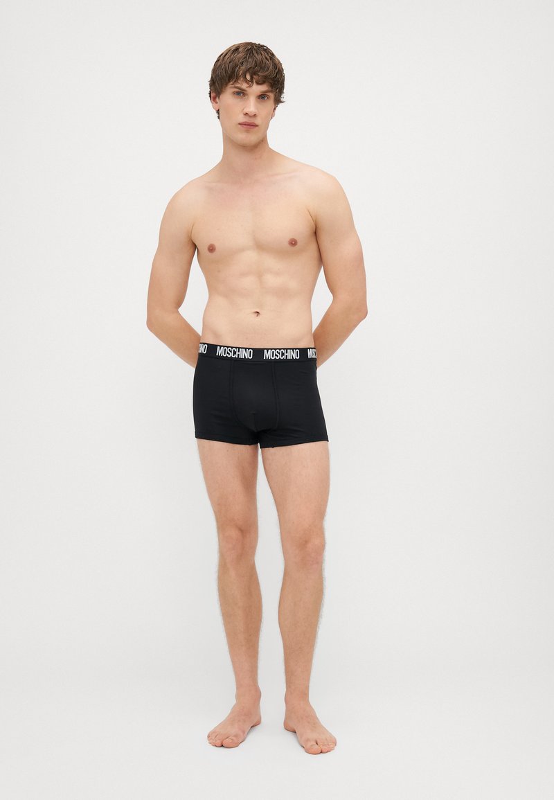 Mustad mustad aluspüksid, mis on valmistatud pehmest kangast. Neil on elastne vöökoht, millel on valgete tähtedega "Moschino", sobiv disain ja nähtamatud mustrid.