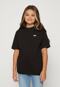 Svart bomull t-shirt med korta ärmar, försedd med en vit Vans-logotyp på vänster bröst; kombinerad med ljusblå denimjeans.