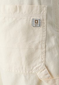 Poche en tissu de couleur crème avec des bords cousus et une petite étiquette de marque rectangulaire indiquant "ONLY & SONS DENMARK ©2013".