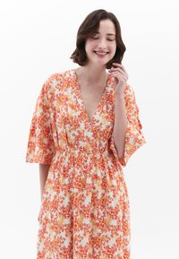 Květinové šaty s hlubokým výstřihem do V, krátkými kimono rukávy a elastickým pasem. Mají oranžový a žlutý květinový vzor na bílém pozadí.