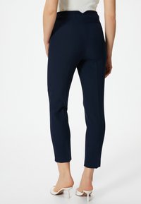 Marineblauwe op maat gemaakte broek met een hoge taille, slanke pasvorm en zijzakken. Het materiaal lijkt glad te zijn en heeft een unieke gegolfde tailleband.