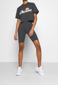Ciemnoszara, krótka koszulka z białym logo "ellesse", w zestawie z pasującymi ciemnoszarymi szortami rowerowymi i białymi butami sportowymi.