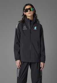 Sort vindjakke med lynlås, med hvide og lyseblå logoer. Sammen med matchende bukser og oversized reflekterende solbriller.