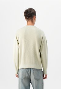 Pulover ribbed de culoare verde deschis, cu gât rotund și umeri căzuți, asortat cu blugi din denim de culoare albastru deschis. Design simplu, casual, cu o textură moale.