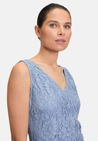 Robe en dentelle bleu clair avec un motif floral, dotée d'un décolleté en V et de larges bretelles. Texture lisse avec des détails complexes.