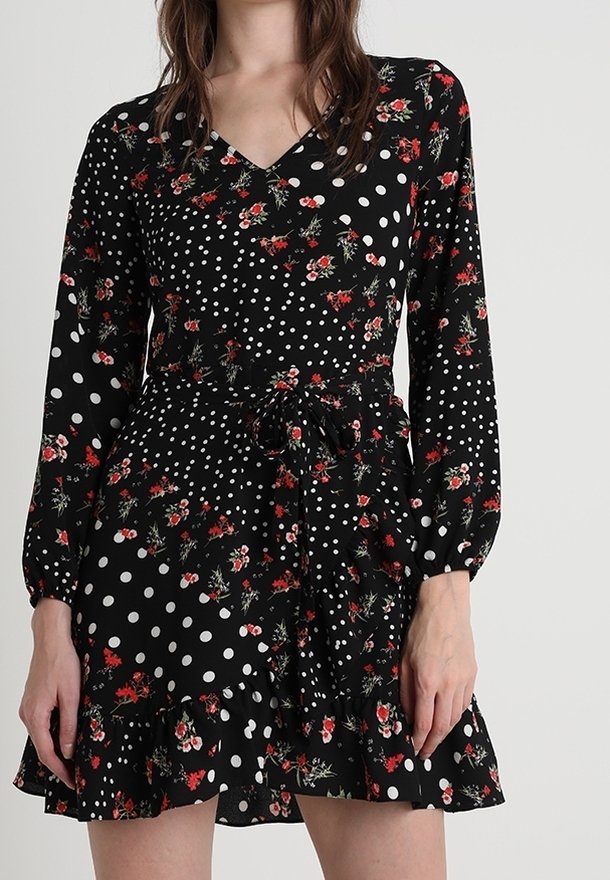 Vestito nero a maniche lunghe, caratterizzato da pois bianchi e motivi floreali rossi; orlo arricciato e cintura annodata in vita.