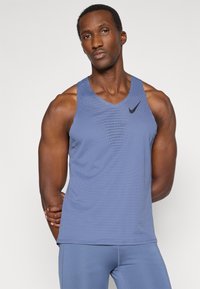 Modrá bezrukávová športová tielko s v-výstrihom, vyrobené z priedušného materiálu s jemným perforovaným vzorom. Čierny akcent loga.