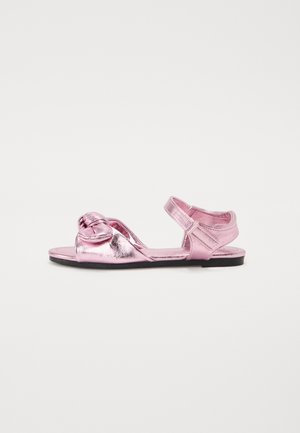 Rosa metallisk sandal med en knyttet detalj foran, åpne sider, justerbar stropp og en flat svart såle. Glatt tekstur.