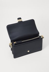 Sac en cuir noir avec rabat ouvert, matériel doré, compartiment zippé et texture lisse. Possède une fermeture à bouton à l'avant.