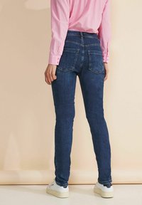 Jeans ajustados de color azul oscuro con cintura alta, con dos bolsillos traseros, combinados con una camisa de botones de manga larga en un tono rosa claro.