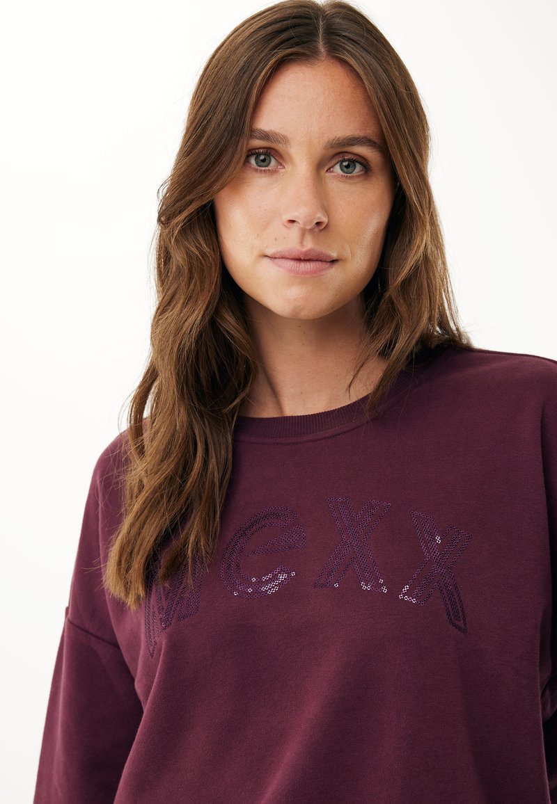 Bordeaux sweatshirts met lange mouwen, ronde halslijn en paillettenletters die "MGXX" in donkerpaars spellen. Gladde stoftextuur.