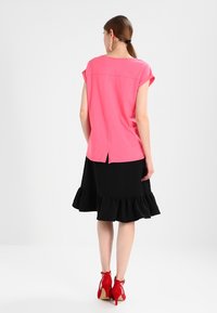 Pink kortærmet top med rygslid, parret med en sort volangnederdel. Røde højhælede sko fuldender outfittet.