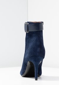 Navyblauwe su ède enkellaars met een gestructureerde zwarte strap en een stilettohak. Gladde afwerking, aangesloten silhouet, minimalistisch ontwerp.